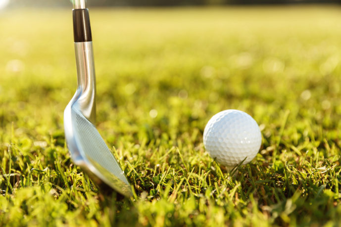 Close up of a golf club and a ball in green grass on a course