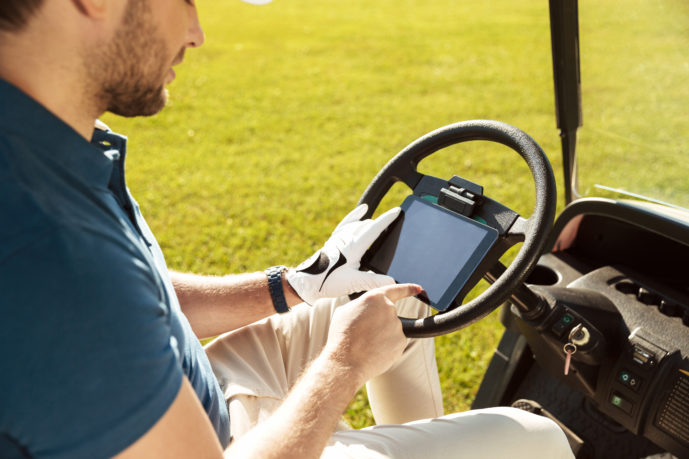 Cropped image of a male golfer sitting in a golf cart and using tablet computer